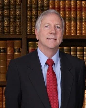William R. Van Order, founding partner, in a dark suit and red tie in front of a bookcase.